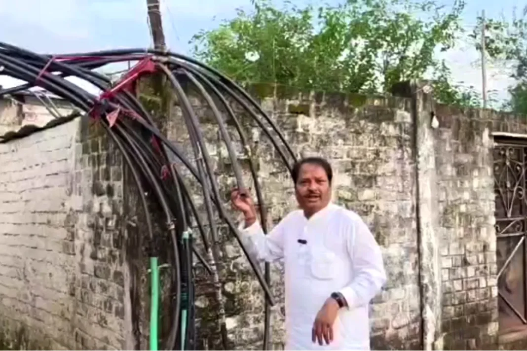 बिजली के खंभों के सहारे हवा में लटकी पानी की पाइपलाइनें